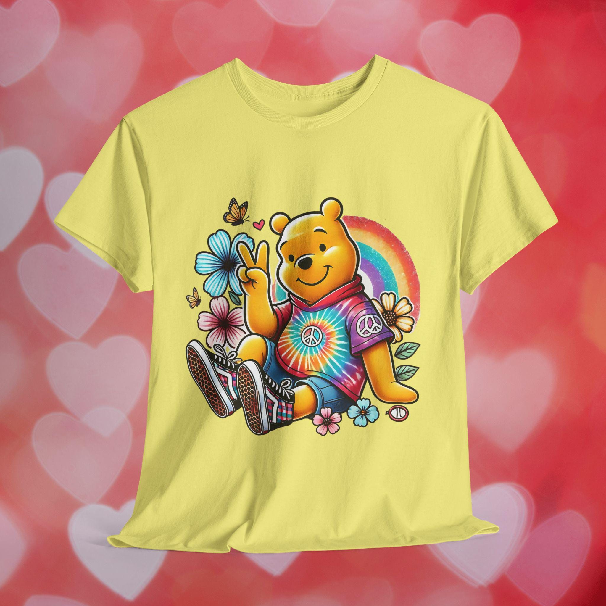 May include: A yellow t-shirt with a cartoon image of Winnie the Pooh wearing a tie-dye shirt and peace sign. Winnie the Pooh is sitting with his legs crossed and holding a peace sign. The shirt has a floral design around Winnie the Pooh.